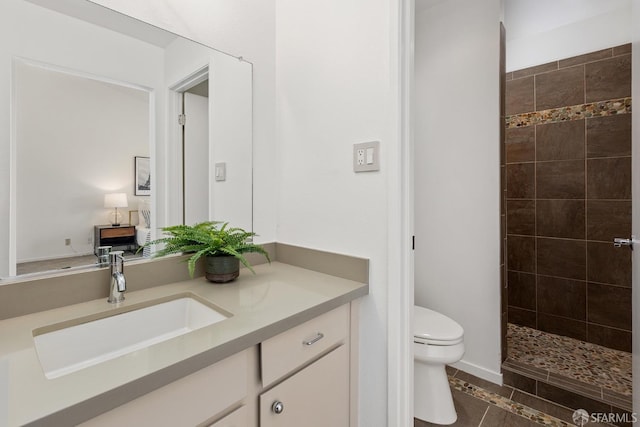 bathroom with tile patterned flooring, a tile shower, vanity, and toilet