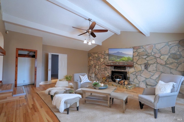 living room featuring light hardwood / wood-style floors, a wood stove, vaulted ceiling with beams, and ceiling fan