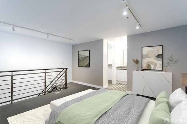 carpeted bedroom featuring ensuite bath, baseboards, and track lighting