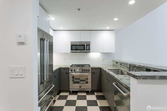 kitchen featuring a sink, dark stone countertops, modern cabinets, high quality appliances, and tile patterned floors