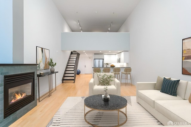 living room with a high ceiling, stairs, rail lighting, a glass covered fireplace, and light wood-type flooring