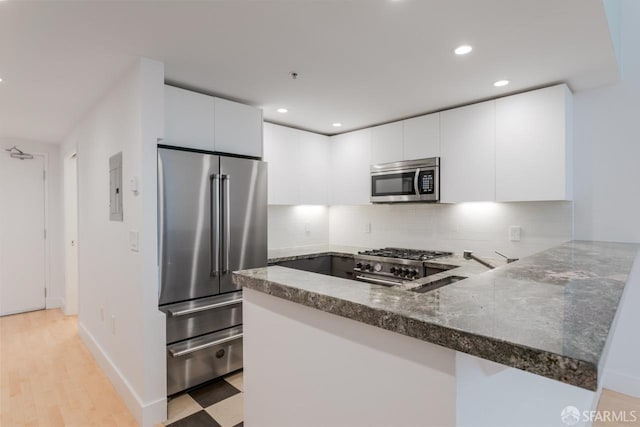 kitchen with a peninsula, high quality appliances, white cabinetry, tasteful backsplash, and dark stone countertops