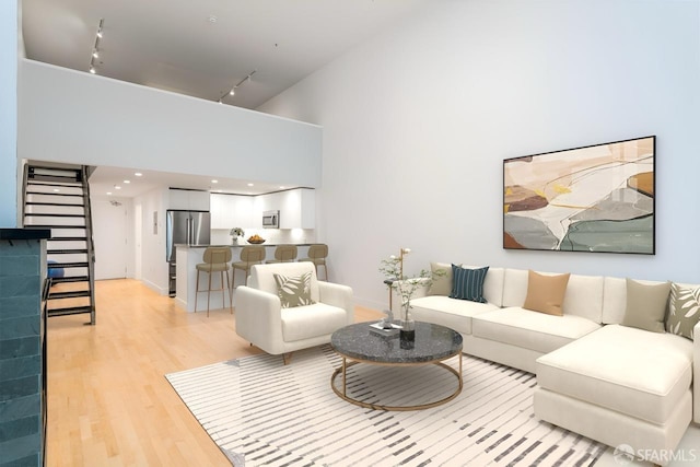 living room with light wood-style floors, stairs, a high ceiling, and track lighting