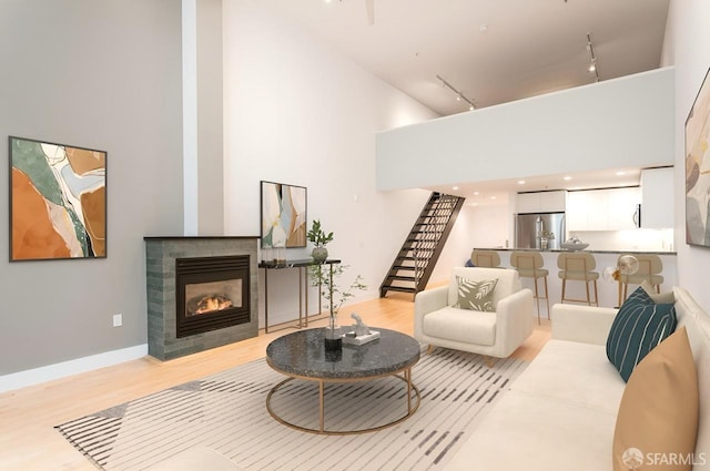 living room featuring a tile fireplace, light wood-style flooring, stairway, rail lighting, and a high ceiling