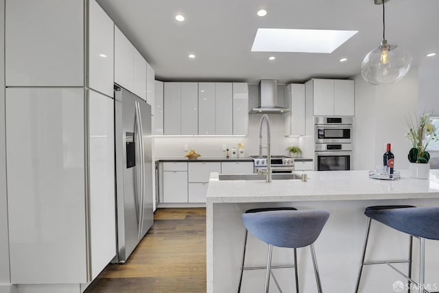 kitchen with white cabinets, wall chimney exhaust hood, stainless steel appliances, and a skylight