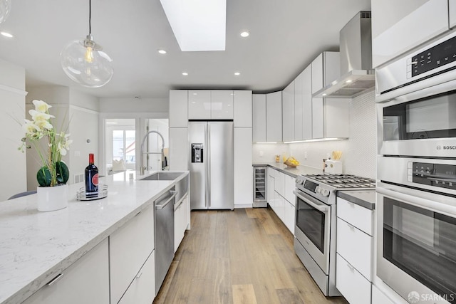 kitchen featuring wine cooler, a skylight, wall chimney exhaust hood, white cabinetry, and stainless steel appliances