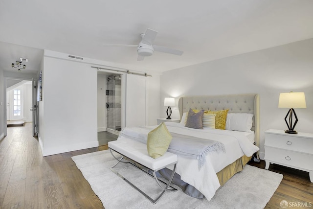 bedroom featuring ceiling fan, a barn door, and dark hardwood / wood-style flooring