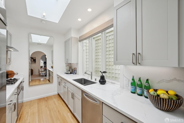 kitchen with sink, a skylight, stainless steel appliances, light hardwood / wood-style floors, and light stone countertops