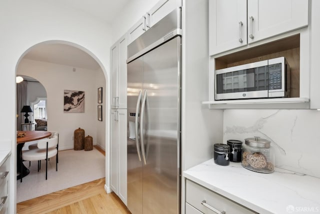 kitchen featuring white cabinetry, decorative backsplash, light parquet floors, light stone counters, and stainless steel appliances