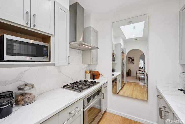 kitchen with light stone countertops, backsplash, stainless steel appliances, and wall chimney exhaust hood