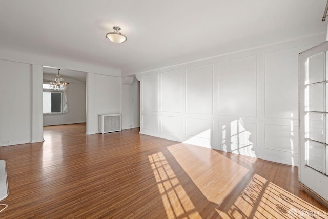 unfurnished living room with a decorative wall, wood finished floors, visible vents, and a chandelier