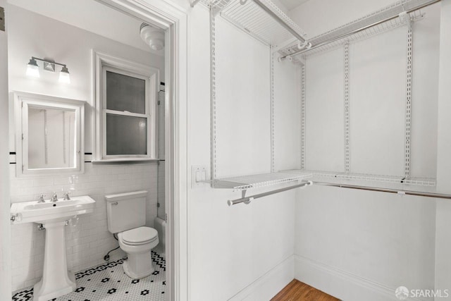 bathroom featuring tile patterned flooring, tile walls, toilet, and a sink