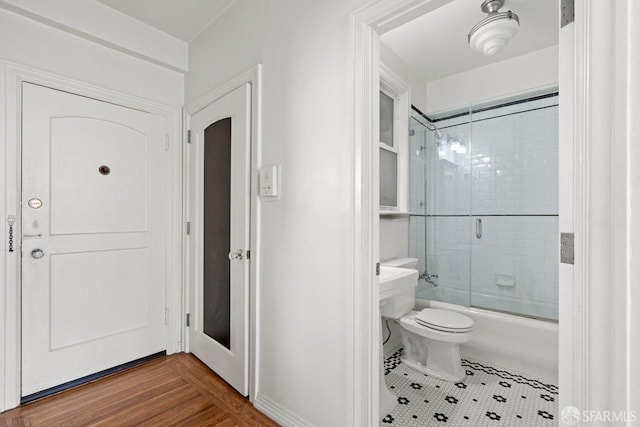 bathroom with toilet, wood finished floors, and bath / shower combo with glass door