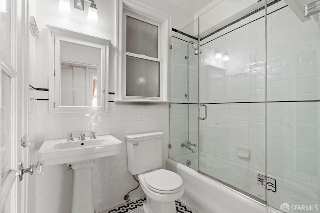 bathroom with enclosed tub / shower combo, toilet, and tile walls