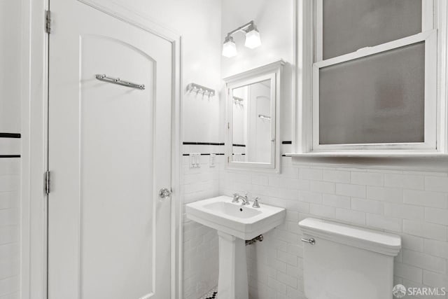 bathroom with tile walls, toilet, a wainscoted wall, and a sink