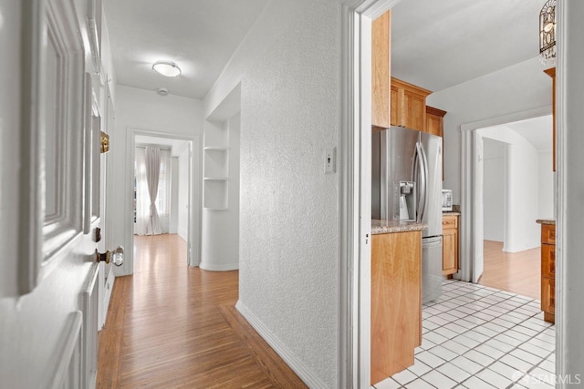 hallway with built in features, light wood-style floors, and a textured wall