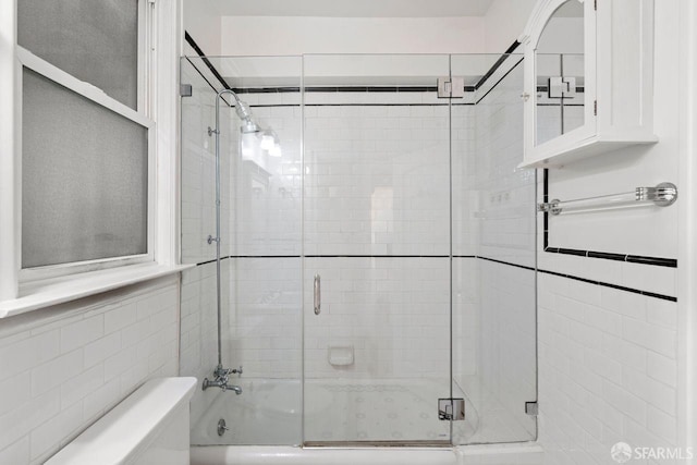 bathroom with toilet and shower / bath combination with glass door