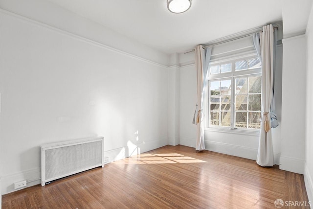 empty room with radiator heating unit, wood finished floors, and a wealth of natural light