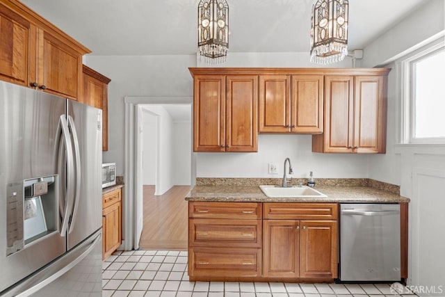 kitchen with a sink, stainless steel appliances, an inviting chandelier, and brown cabinetry