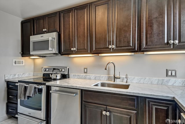 kitchen featuring sink, dark brown cabinetry, light stone countertops, and appliances with stainless steel finishes