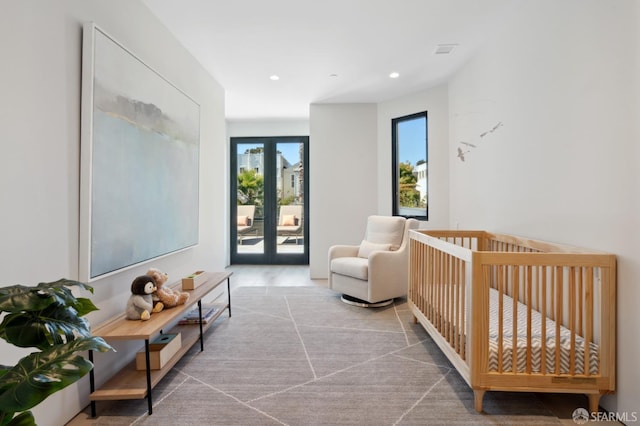 bedroom with a nursery area, french doors, access to outside, and light hardwood / wood-style flooring