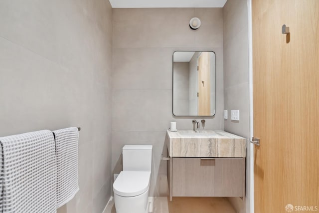 bathroom featuring vanity, toilet, and tile walls