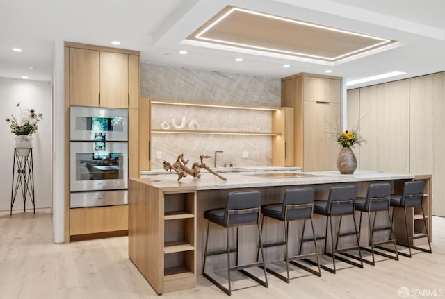 kitchen with double oven, light stone countertops, light brown cabinets, and light hardwood / wood-style floors