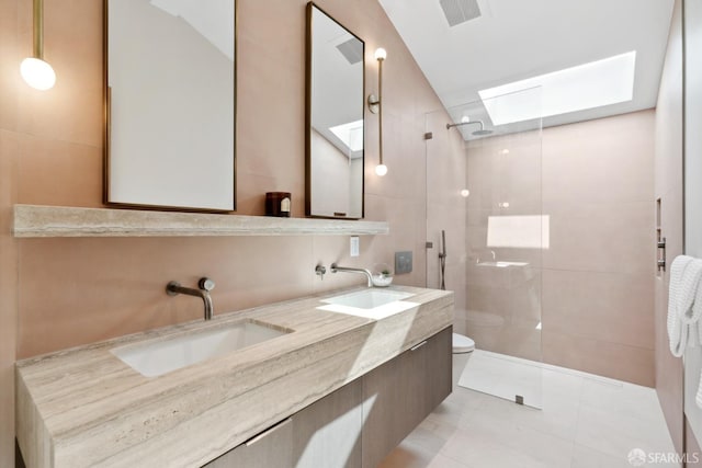 bathroom with a skylight, a tile shower, vanity, tile patterned flooring, and toilet