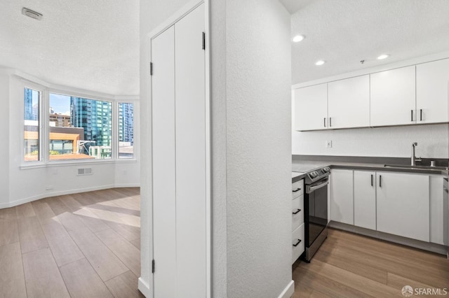 kitchen featuring sink, white cabinetry, stainless steel electric range, a textured ceiling, and light hardwood / wood-style floors