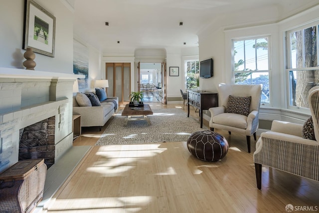 living room with light wood-type flooring, plenty of natural light, ornamental molding, and a stone fireplace