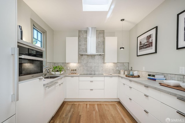 kitchen with oven, white cabinets, pendant lighting, and wall chimney exhaust hood