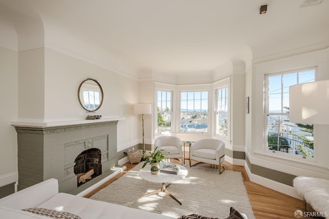 interior space featuring ornamental molding, light wood-type flooring, a brick fireplace, and plenty of natural light