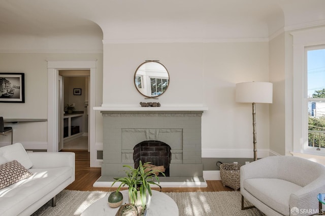 living room featuring ornamental molding, a brick fireplace, and wood-type flooring