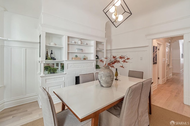 dining area featuring a wainscoted wall, vaulted ceiling, light wood finished floors, built in features, and a decorative wall