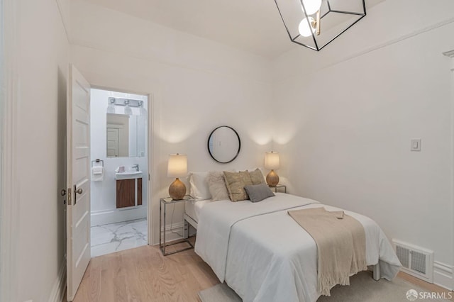 bedroom with connected bathroom, baseboards, visible vents, and light wood finished floors