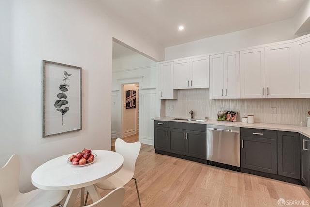 kitchen featuring white cabinetry, light countertops, stainless steel dishwasher, a sink, and light wood-style floors