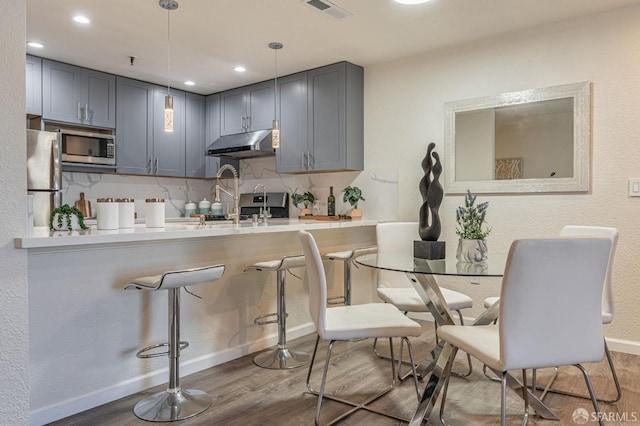1396 El Camino Real Unit 110, Millbrae, CA 94030 - kitchen with appliances with stainless steel finishes, under cabinet range hood, wood finished floors, gray cabinets, and a kitchen bar