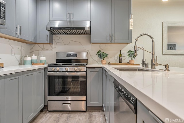 1396 El Camino Real Unit 110, Millbrae, CA 94030 - kitchen featuring stainless steel appliances, wall chimney exhaust hood, gray cabinetry, light wood-type flooring, and light stone countertops