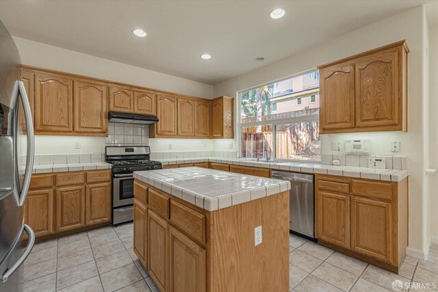 kitchen with appliances with stainless steel finishes, light tile patterned floors, sink, tile countertops, and a center island