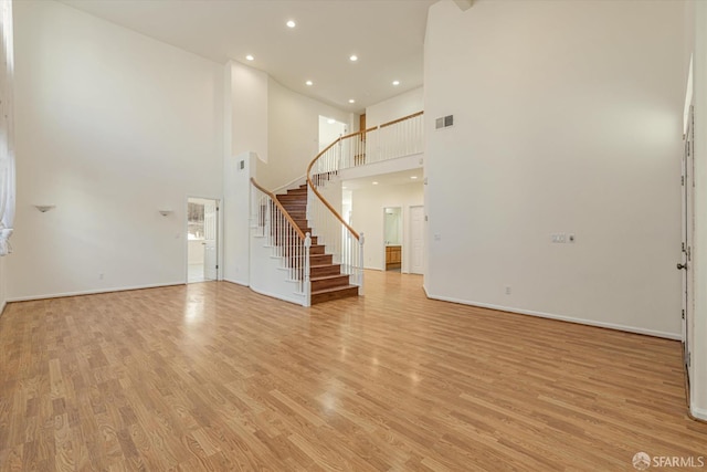 unfurnished living room with light hardwood / wood-style flooring and a towering ceiling