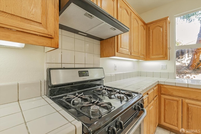 kitchen with ventilation hood, light tile patterned floors, black gas range, decorative backsplash, and tile counters