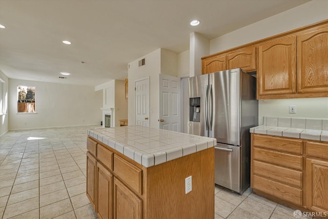 kitchen with stainless steel refrigerator with ice dispenser, tile countertops, light tile patterned flooring, and a center island