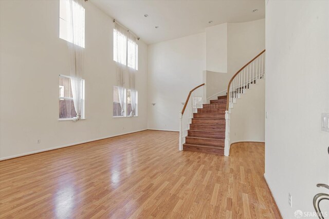 unfurnished living room featuring a towering ceiling and light hardwood / wood-style flooring