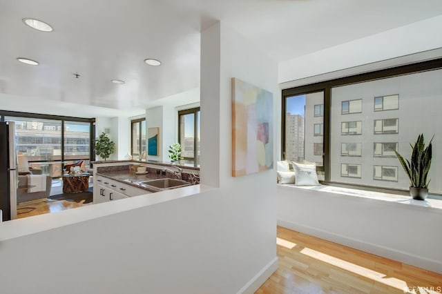 kitchen with white cabinets, stainless steel fridge, light wood-type flooring, and sink