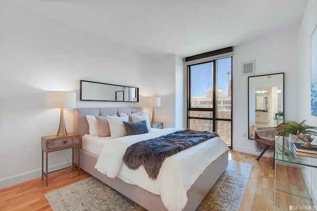 bedroom with expansive windows, light wood-type flooring, and connected bathroom