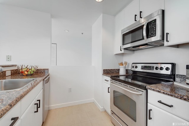 kitchen with sink, stainless steel appliances, light tile patterned floors, dark stone countertops, and white cabinets