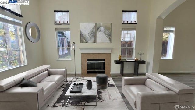 living room featuring a tiled fireplace, plenty of natural light, wood-type flooring, and a high ceiling