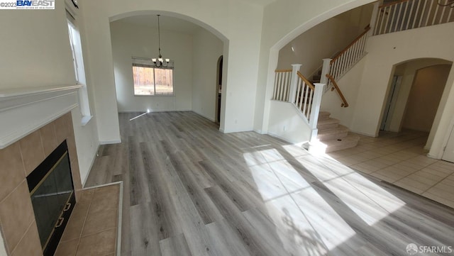 unfurnished living room featuring a tile fireplace, a towering ceiling, light hardwood / wood-style floors, and a notable chandelier