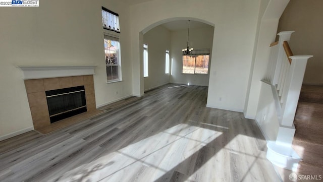 unfurnished living room featuring hardwood / wood-style flooring, a chandelier, and a tiled fireplace