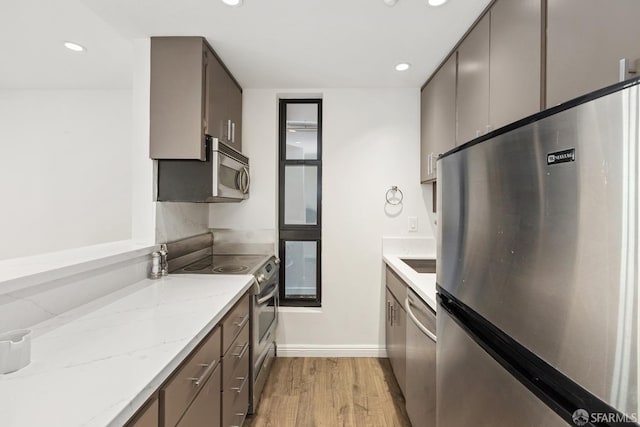 kitchen featuring sink, stainless steel appliances, light hardwood / wood-style flooring, and light stone counters